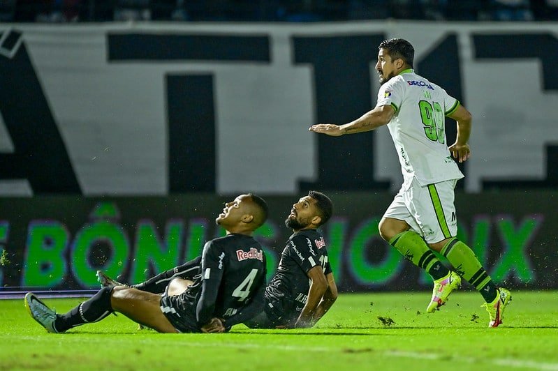 Foto mostra Aloísio, do América-MG, de pé, e dois jogadores do Bragantino no chão (foto: Mourão Panda/América-MG)