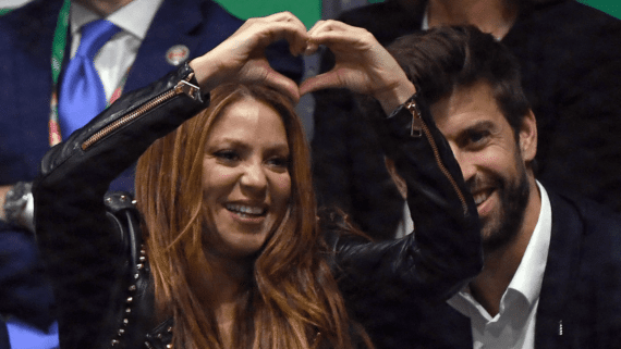 Shakira fazendo coração com as mãos; Piqué aparece ao fundo (foto: Gabriel Bouys/AFP)