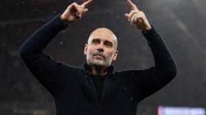 Guardiola com roupa preta e de braços levantados (foto: Divulgação/Manchester City)