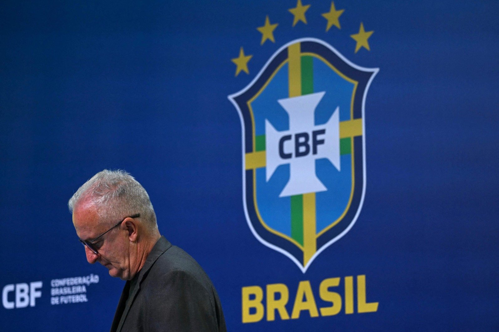 Técnico Dorival Júnior cabisbaixo com o símbolo da CBF ao fundo (foto: Mauro Pimentel/AFP)