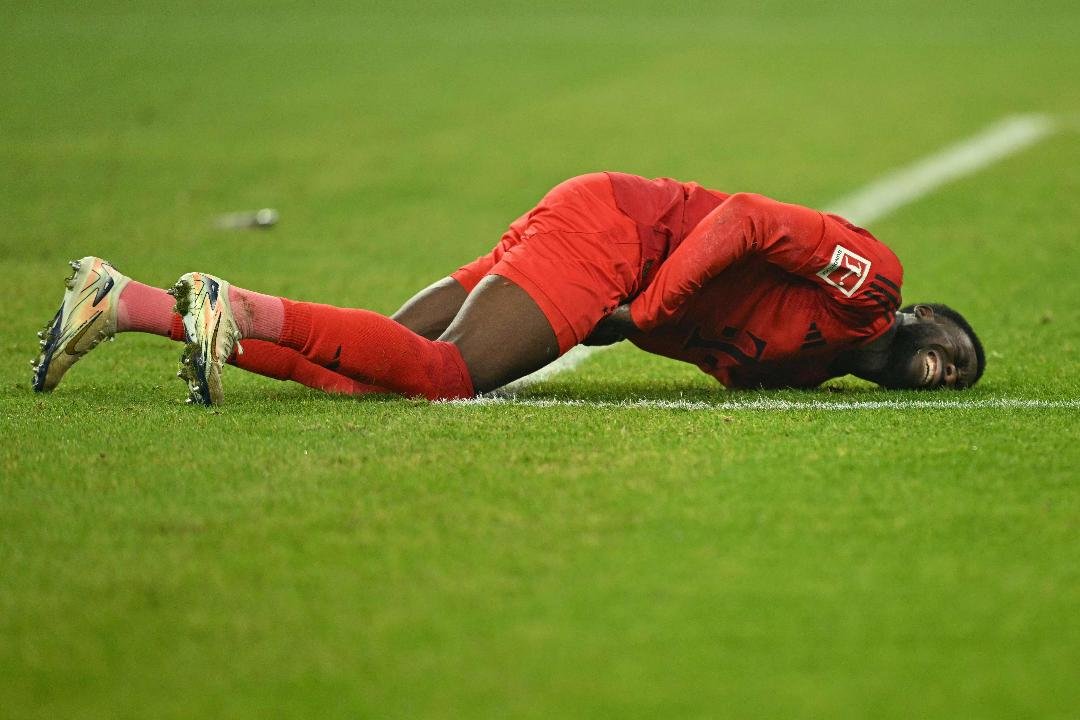 Alphonso Davies deitado no chão em partida pelo Bayern de Munique (foto: INA FASSBENDER / AFP)