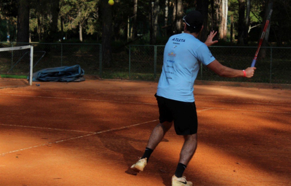 homem jogando tênis em quadra de saibro (foto: DYNAMIS SOCIAL/Divulgação)