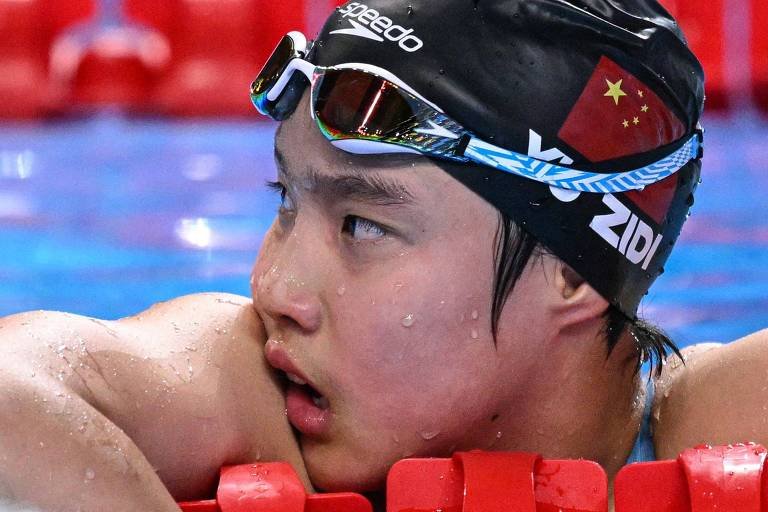 Yu Zidi se apóia nas raias da piscina após as semifinais dos 200 metros borboleta no Mundial em Singapura (foto: Oli Scarff - 30.jul.2025/AFP)
