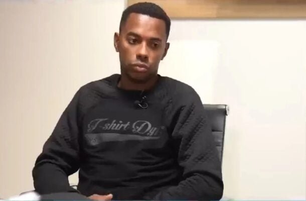 Ex-jogador de futebol Robinho sentado olhando para baixo de moletom preto (foto: Foto: Reprodução/Globoplay)