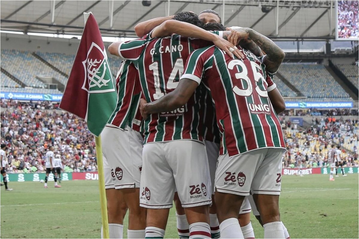 Jogadores do Fluminense comemorando um gol com um abraço em grupo do lado da bandeira de escanteio do clube. (foto: Divulgação/Fluminense)