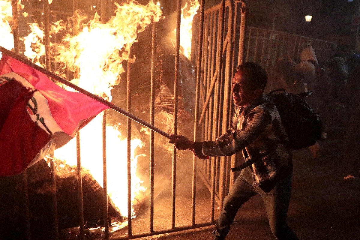 Manifestantes carrega bandeira do Peru ao lado de fogo durante protesto em Lima, no Peru