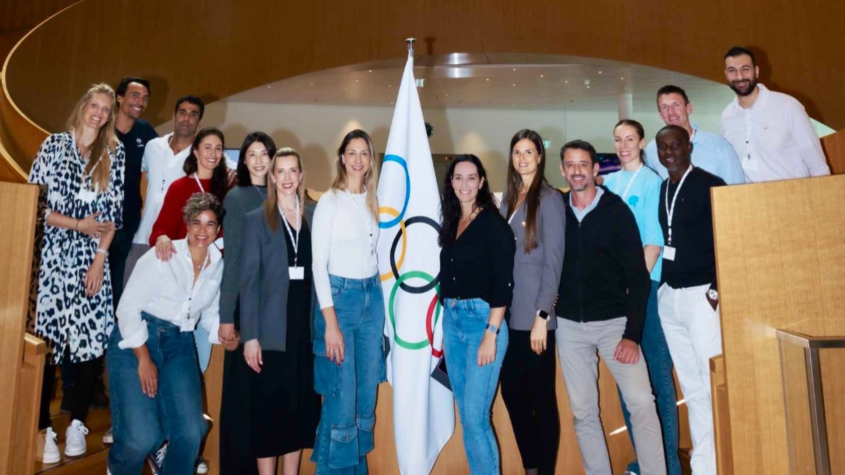 Carol Gattaz e outros participantes do curso 'além da quadra' posam ao lado de bandeira olímpica (foto: Divulgação/FIVB)