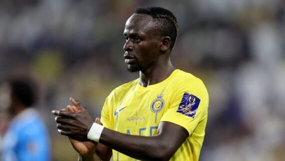 Homem negro em camisa de futebol amarela Al-Nassr, distintivos, mãos unidas, olhando para o lado. (foto: Divulgação)